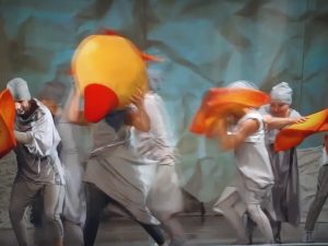 Zdjęcie fragmentu przedstawienia. Aktorzy ubrani na biało poruszają się trzymając w dłoniach fragmenty kukiełki ptaka.