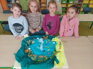 Cztery uczennice stoja przy stoliku, na którym ustawiono wykonaną przez nie kolorowa makiete przedstawiająca jezioro.