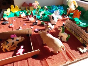 Zdjęcie fragmentu makiety przedstawiającej zagrodę z ustawionymi figurkami zwierząt.