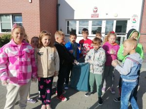 Uczniowie pozują do zdjęcia grupowego przed budynkiem szkoły. Dwóch chłopców stojących po srodku trzyma niebieski worek ze śmieciami.