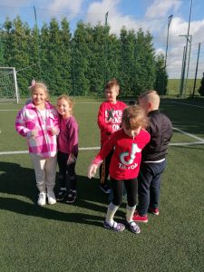 Piatka dzieci podczas sprzatania świata stoi na murawie szkolnego orlika. Dwie dziewczynki stojące obok siebie usmiechają się do zdjęcia.