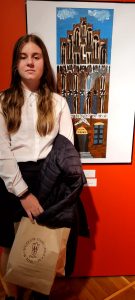 Zdjęcie nagrodzonej uczennicy stojacej na tle swojej pracy.