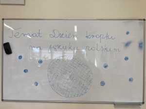 Zdjęcie tablicy szkolnejz napisem: Temat: Dzień kropki na języku polskim. Wokół napisu narysowano różnej wielkości kropki.