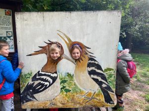 Dwoje uczniów pozuje do zdjęcia . w obrazie przestawiającym dwa ptaki zwrócone głowami do siebie wycięte są otwory w miejscu ich głów, w których widać głowy uczniów.