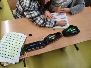 Dwie uczennice siedzace przy szkolnym stoliku zakreślaja kropki na leżącej przed nimi kartce.