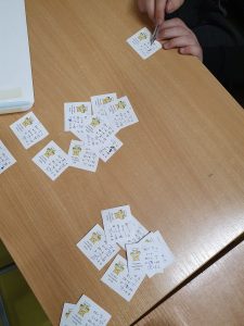 Zdjęcie biurka na którym leżą karteczki z działaniami wykonanymi przez uczniów. Na zdjęciu widać jak jeden z uczniów sprawdza zadania.