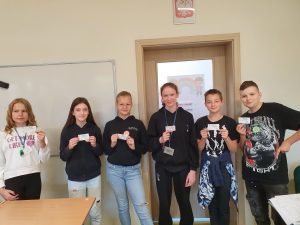 Uczniowie klasy szóstej pozują do zdjęcia z odznakami i certyfikatami mistrza tabliczki mnożenia otrzymanymi za poprawne wykonanie działań.
