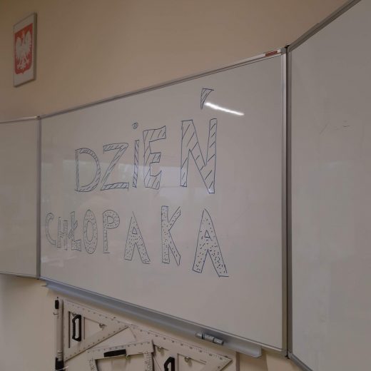 Zdjęcie białekj szkolnej tablicy z odrecznym napisem :"DZIEŃ CHŁOPAKA"