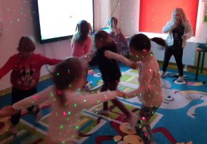 Uczniowie oddziału przedszkolnego podczas tańców w swojej klasie. Na dzieciach i scianach widać kolorowe laserowe światełka.