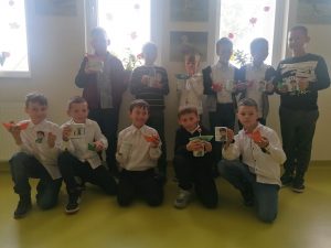 Uczniowie klasy trzeciej pozują do zdjęcia z otrzymanymi prezentami - kubkami i łudeczkami z papieru ozdobionymi lizakami.