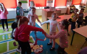 Uczniowie oddziału przedszkolnego podczas tańców w swojej klasie. Na dzieciach i scianach widać kolorowe laserowe światełka.