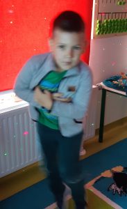 Uczeń oddziału przedszkolnego podczas tańca w sali lekcyjnej. Chłopca otaczają kolorowe laserowe światełka. Zdjęcie jest lekko rozmazane.