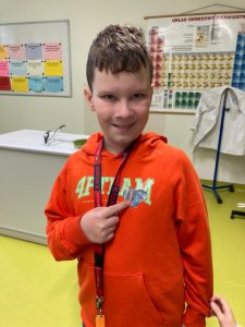 Uczeń pozuje do zdjęcia. Palcem u prawej dloni wskazuje serduszko przyczepione do jego bluzy.