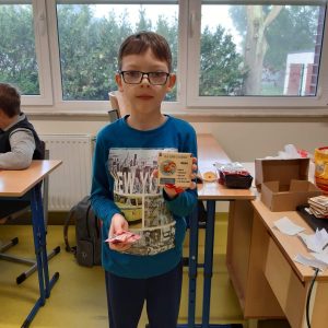 Uczeń pozuje do zdjęcia z otrzymanym z okazji dnia chłopaka prezentem - drewnianym pudełkiem z napisem Olek i kolorowym obrazkiem.