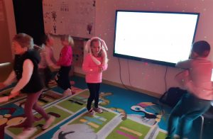 Uczniowie oddziału przedszkolnego podczas tańców w swojej klasie. Na dzieciach i scianach widać kolorowe laserowe światełka.