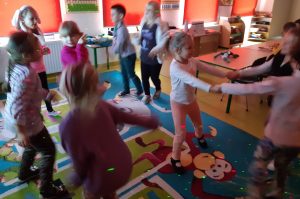 Uczniowie oddziału przedszkolnego podczas tańców w swojej klasie. Na dzieciach i scianach widać kolorowe laserowe światełka.