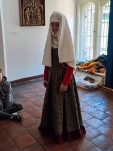 Uczennica klasy piątej stoi w stroju mieszczańskim z epoki. Ma założoną długą suknię a na głowie biały czepek całkowicie zasłaniający jej głowę.