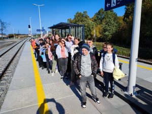 Uczniowie klasy piątej stoją w grupie na peronie w oczekiwaniu na pociąg.