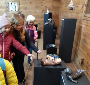 Uczniowie oddziału przedszkolnego podczas zwiedzania wystawy w Muzeum Etnograficznym. Dzieci przyglądają się eksponatom. Dziewczynki wyciągają ręce tak jakby chciały dotknąć jeden z eksponatów.