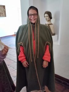 Uczennica klasy piątej uśmiecha się do zdjęcia. Dziewczynka przebrana jest w zielony żupan z kapturem naciągniętym na głowę i zawiązanym pod szyją.