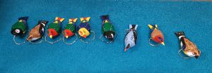 Zdjęcie ustawionych obok siebie na niebieskiej podstawce kolorowych ptaszków wykonanych z drewna.