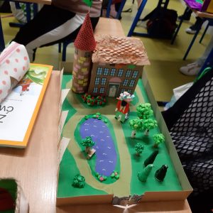 Zdjęcie makiety akademmii Pana Kleksa wykonanej przez ucznia klasy czwartej. makieta ustawiona jest na stole, przedstawia buden z wieloma oknamia przed nim ustawiono drzewa, staw i postać Pana Kleksa.