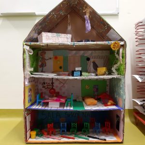 Zdjęcie makiety akademii Pana Kleksa wykonanej przez ucznia klasy czwartej. Makieta przedstawia przekrój 4 piętrowego budynku ze spadzistym dachem. Wnętrze budynku zaopatrzone jest w miniaturowe mebelki i kolorowe ściany.