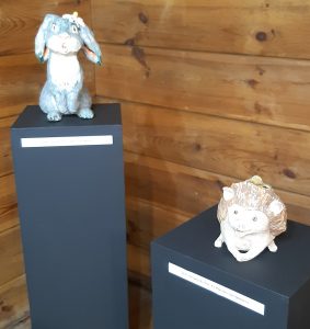 Zdjęcie eksponatów Muzeum Etnograficznego w Toruniu. Na wystawie figurki zająca i jeża stojące na osobnych wzniesieniach.