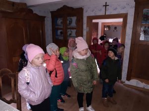 Uczniowie w kurtkach i czapkach stoją w pomieszczeniu muzeum z drewnianymi meblami.