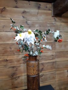 Zdjęcie ekspozycji w muzeum etnograficznym - w drewnianym wazonie kompozycja z jarzębiny i białych kwiatów z żółtymi środkami.
