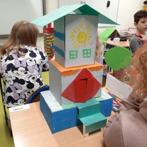 Zdjęcie makiety Akademii Pana Kleksa wykonanej przez jedną z uczennic klasy czwartej. Makieta przedstawia kolorowy domek ze spadzistym dachem i schodkami do niego prowadzącymi. Ściany budynku ozdobiono kolorowymi rysunkami.