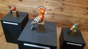 Zdjęcie eksponatów Muzeum Etnograficznego w Toruniu. Na wystawie trzy kolorowe ptaszki wykonane z drewna.