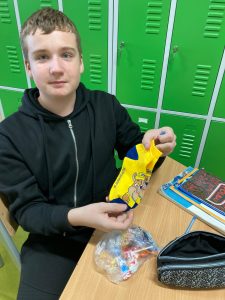 Uczeń klasy siódmej siedzi przy ławce. Prezentuje otrzymane z okazji dnia chłopaka skarpetki trzymane w dłoniach.