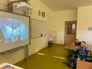 Uczniowie siedzą w ławkach klasowych i oglądają wyświetlany na projektorze film.