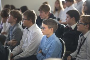 Uczniowie siedzą na krzesełkch na sali gimnastycznej podczas wystąpienia łukasza Kazka. Uczniowie patrzą się w jedną stronę i wyglądają na zasluchanych.