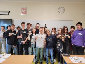 Uczniowie klasy ósmej pozują do zdjęcia z odznakami i certyfikatami mistrza tabliczki mnożenia otrzymanymi za poprawne wykonanie działań.