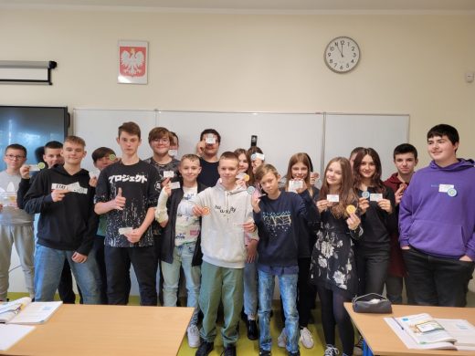 Uczniowie klasy ósmej pozują do zdjęcia z odznakami i certyfikatami mistrza tabliczki mnożenia otrzymanymi za poprawne wykonanie działań.