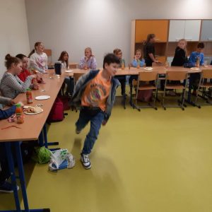 Uczeń klasy czwartej podczas biegu wokół sali. W tle widac siedzących przy wspólnym stole pozostałych uczniów.