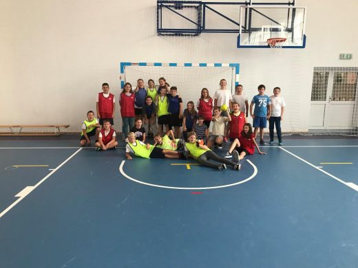 Uczniowie klasy piatej w strojach sportowych pozują do wspólnego zdjęcia na tle bramki piłkarskeij na szkolnej sali gimnastycznej.