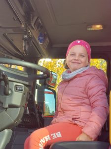 Uczennica klasy pierwszej siedzi za kierownicą wozu strażackiego. Dziewczynka uśmiecha się do zdjęcia.