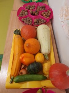 Na tackach ustawionych w rzędzie na stojących pod ścianą stolikach, ułożono różnego rodzaje dynie oraz orzechy włoskie.