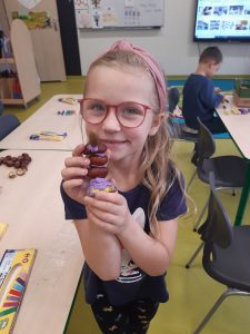 Uczennica oddziału przedszkolnego trzyma w dłoniach figurkę zbudowaną z plasteliny i kasztanów.