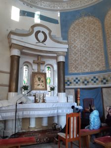 Zdjęcie ołtarzu wewnątrz okrągłej kapliczki zwiedzanej przez uczniów. Na białym ołtarzu ustawiono obraz Matki Bożej a nad nim krzyż. Ołtarz zwieńczają dwie brązowej kolumny połączone białym, ozdobnym wspornikiem.