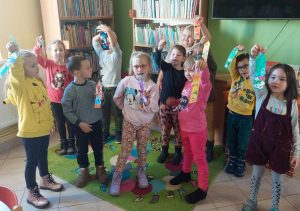 Dzieci z oddzialu przedszkolnego stoją w gromadzie i podnoszą w górę kolorowe zakładki.