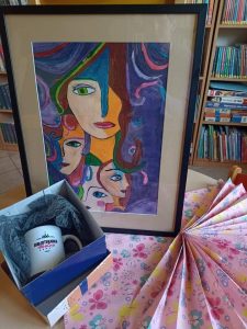 Zdjęcie prezentu otrzymanego przez Panią Monikę od Szkoły Podstawowej w Ostaszewie - oprawiona w ramkę praca jedenj z uczennic oraz kubek z dedykacją w granatowym pudełku.