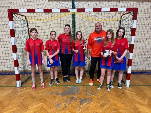 Uczennice wraz z nauczycielem wychowania fizycznego stoją w czerwono-niebieskich strojach w bramce do piłki nożnej.