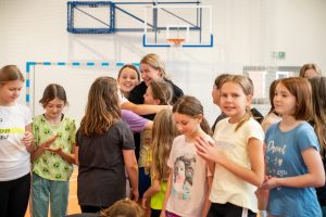 Adrianna Sułek w uścisku z dwoma uczennicami klasy piatej. Obok widać stojących innych uczniów.