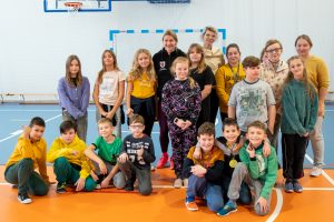 Adrianna Sułek pozuje do zdjęcia z uczniami klasy czwartej. Częśc uczniów kuca na sali gimnastycznej.