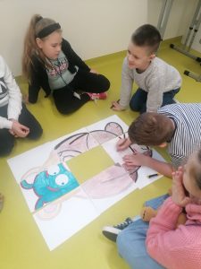 Uczniowie składają misia z puzli recznie pomalowanych kredkami. Każdy puzel stanowi osobna kartka papieru.