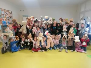 Uczniowie klas 1 - 3 pozują do grupowego zdjęcia ze swoimi pluszowymi misiami, które trzymają w rękach.